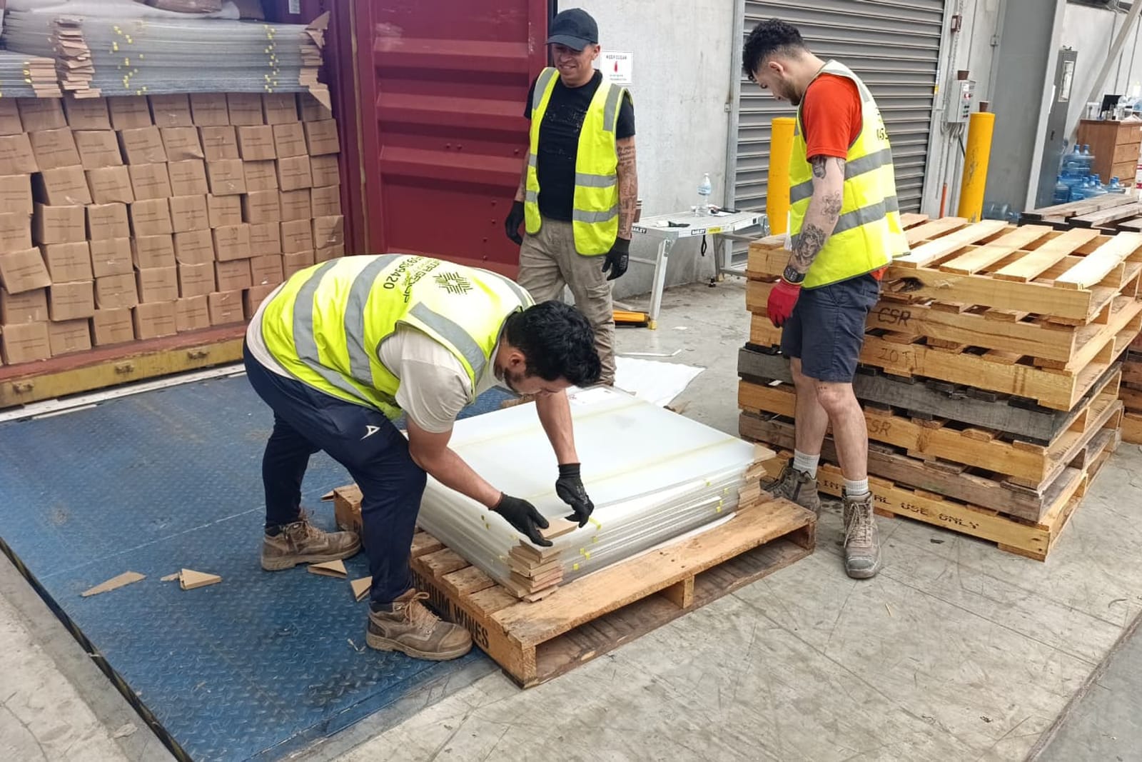Three Calima workers loading sheet stock onto pallets at a client site
